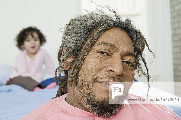 Porträt eines lächelnden erwachsenen Mannes mit seiner hinter ihm sitzenden Tochter