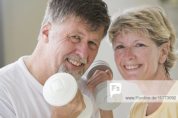 Porträt eines älteren Paares  das mit Handgewichten trainiert und lächelt