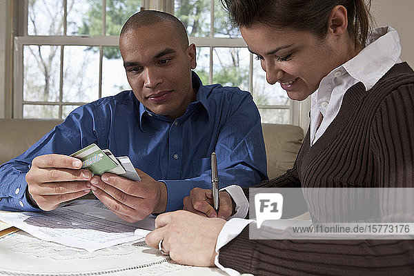 Ein junges Paar überprüft seine Finanzen an einem Tisch zu Hause mit Kreditkarten und Notizen