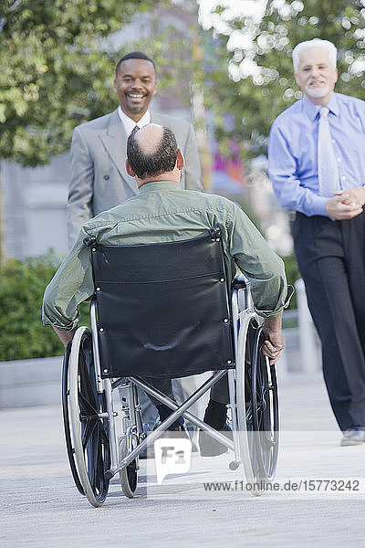 Zwei lächelnde Geschäftsleute und ein Mann im Rollstuhl im Freien