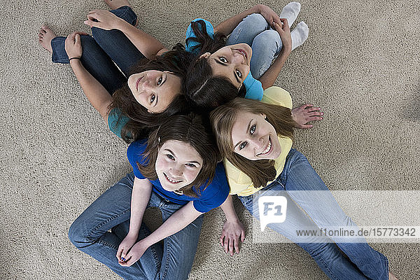 Portrait of four teenage girls sitting on the floor at home and looking up at the camera
