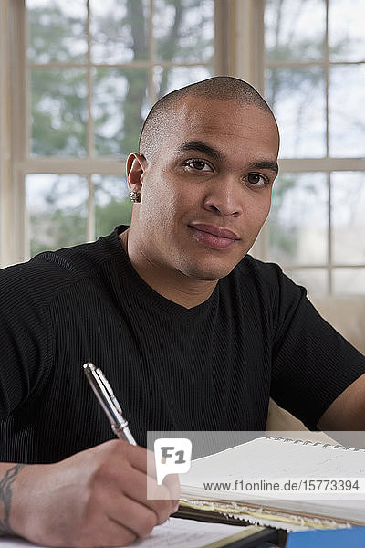 Male college student sitting at home making notes in a notebook for homework