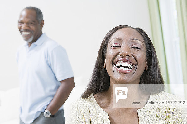 Porträt einer lächelnden Frau mittleren Alters mit einem im Hintergrund stehenden Mann mittleren Alters