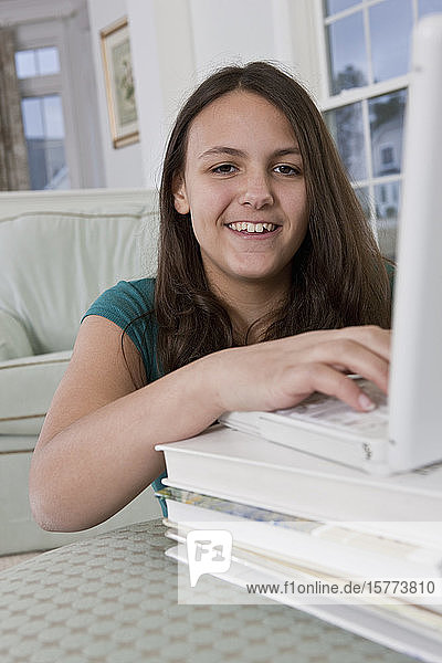 Teenager-Mädchen  das einen Laptop benutzt  der auf Lehrbücher gestützt ist und in die Kamera schaut