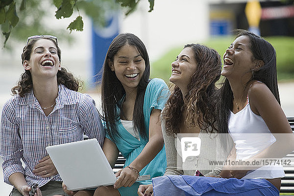 Four teenage girls sitting on a bench and smiling in the school campus