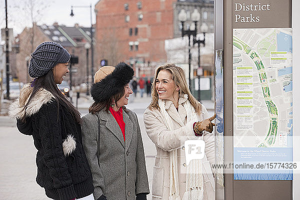 Three women standing outdoors and looking at a city map and advertisement; Boston  Massachusetts  United States of America