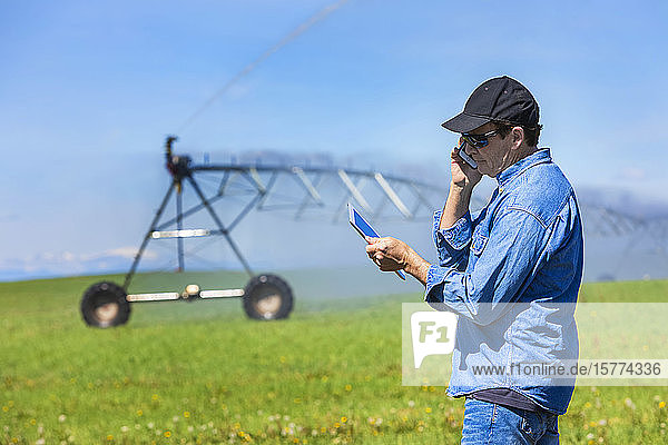 Farmer using a tablet and smart phone on a farm field with irrigation; Alberta  Canada