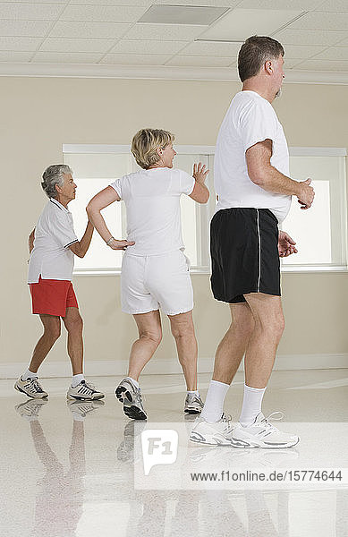 Zwei ältere Frauen und ein älterer Mann trainieren in einem Fitnessstudio