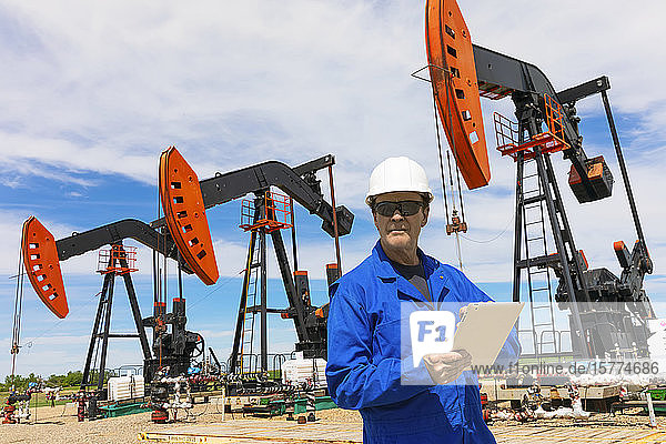 Man working on a tablet with pumpjacks in the background; Alberta  Canada