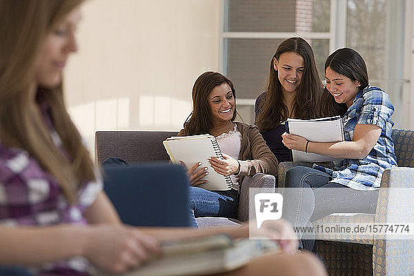 Four teenage girls in a high school corridor  looking through notebooks together
