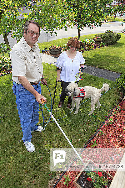 A woman with a disability at home with her husband  standing in the yard with walking aids and a service dog