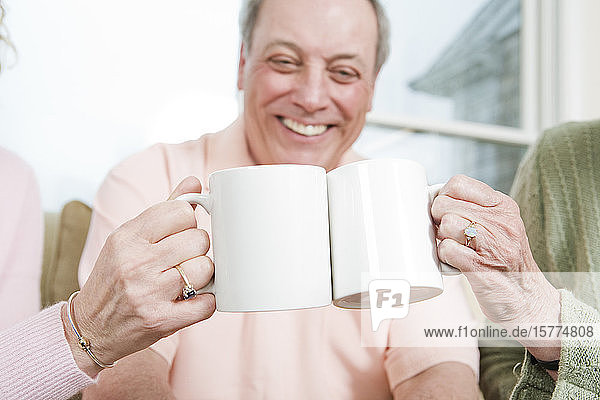 Älterer Mann lächelt mit zwei Frauen  die Kaffeetassen im Vordergrund halten.