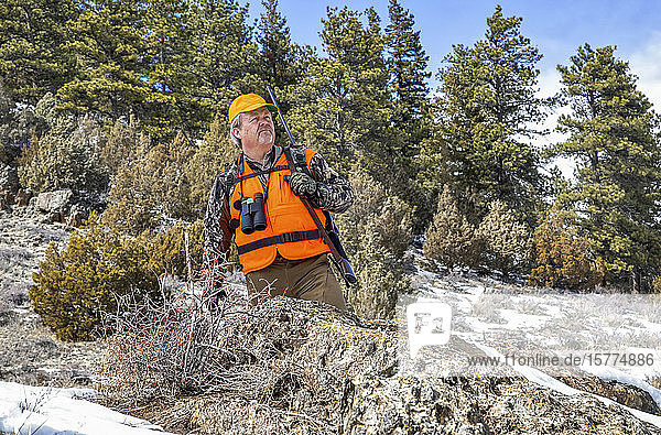 Jäger mit orangefarbener Weste  Fernglas und Gewehr steht auf einem Hügel und schaut hinaus; Denver  Colorado  Vereinigte Staaten von Amerika