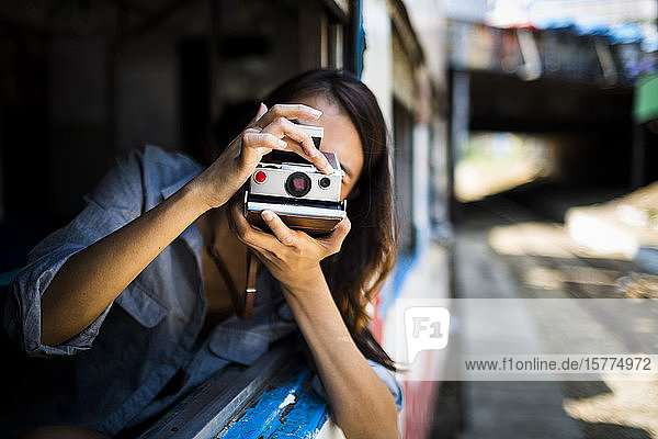 Junge Frau fährt in einem Zug  schaut aus dem Fenster und fotografiert mit einer alten Polaroidkamera.
