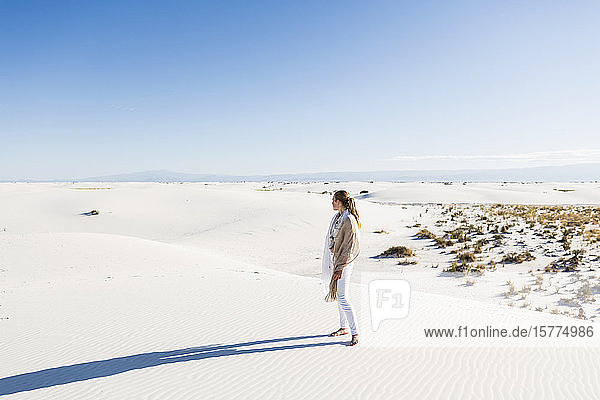 A teenage girl standing looking at a vast open space of sand dunes.