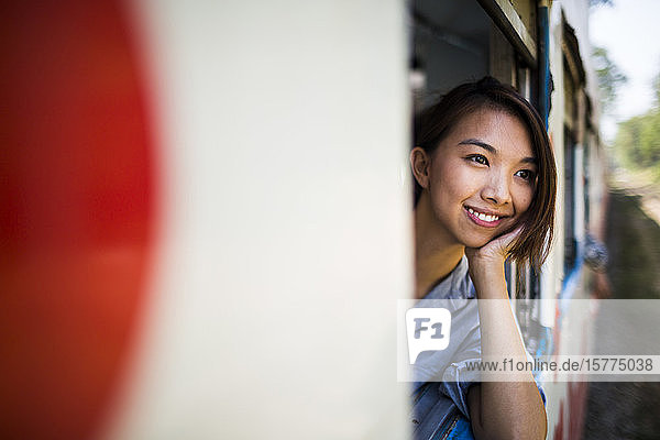 Lächelnde junge Frau in einem Zug  die aus dem Fenster schaut.