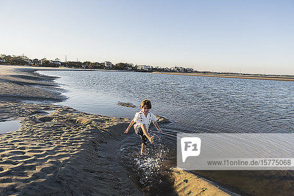 A six year old boy on the beach splashing in shallow water