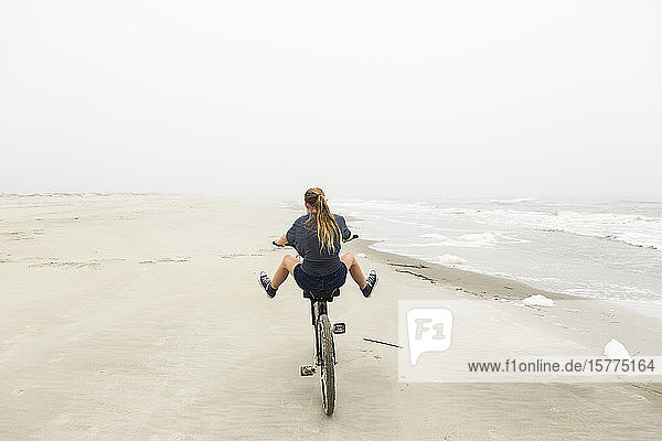 Teenage girl riding a bike on sand at the beach