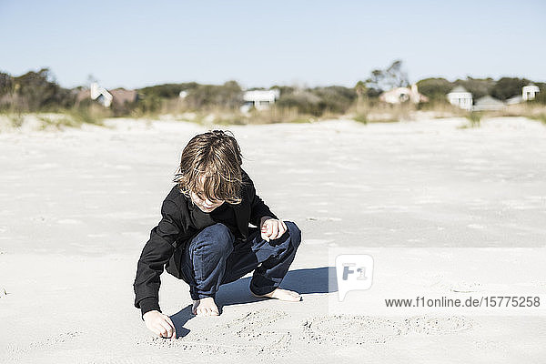 A six year old boy drawing in the soft white sand on the beach