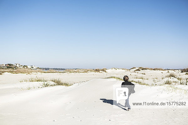 Ein sechsjähriger Junge  der im Freien über Sanddünen läuft.
