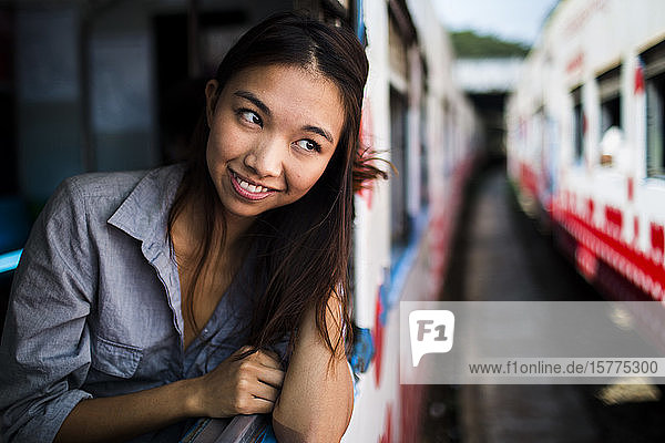 Lächelnde junge Frau in einem Zug  die aus dem Fenster schaut.