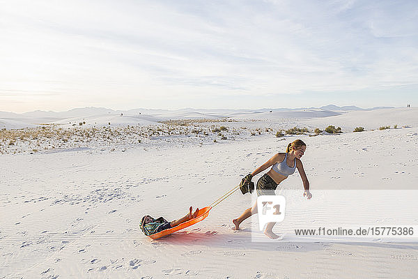 A teenage girl pulling her brother in sled at sunset