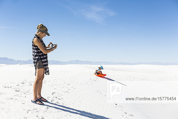 Mother taking picture of son sledding on sand dunes