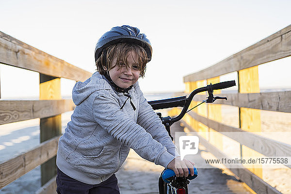 Ein Junge auf einem Fahrrad  mit Helm auf einem Gehweg am Strand