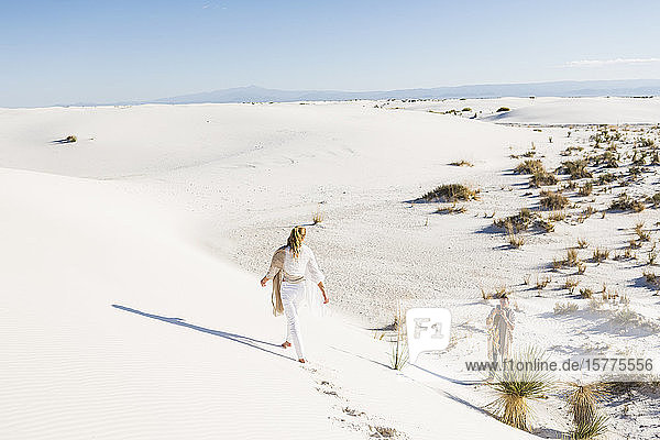 A teenage girl walking across sand dunes leaving footprints