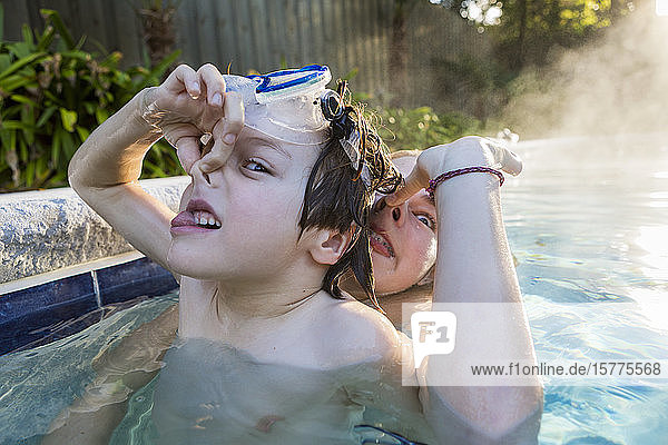 Ein Junge und seine Schwester spielen im frühen Morgenlicht im Pool  ein Junge hält sich die Nase zu.
