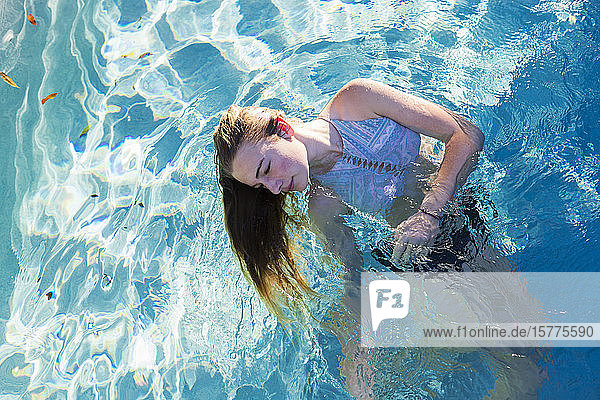 Ein Teenager-Mädchen schwimmt in einem Pool  die Haare am Hinterkopf schwimmen im Wasser.