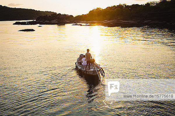 Hochwinkelaufnahme eines Mannes  der bei Sonnenaufgang ein kleines Boot auf eine Insel steuert.