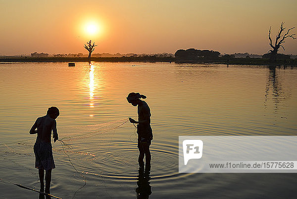 Two boys fishing in a lake at sunset  Amapura  Myanmar.