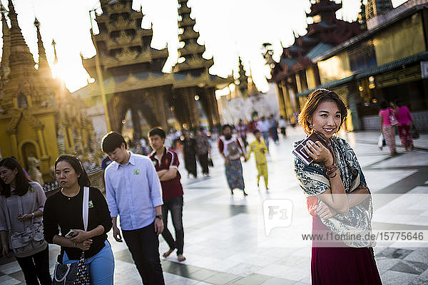 Young woman standing in town square  holding old Polaroid camera  pagoda in the background.
