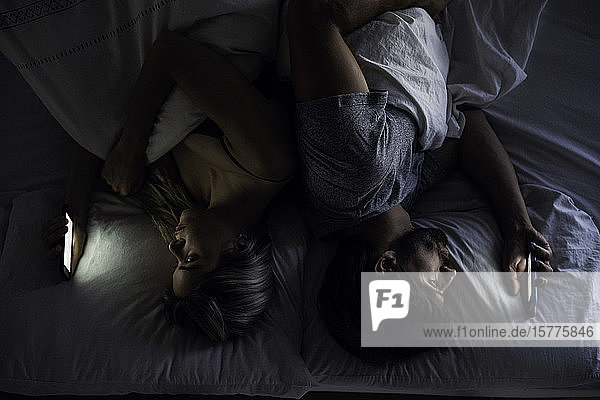 Junges Paar benutzt Smartphones auf dem Bett