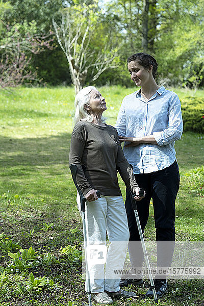 Pflegerin und ältere Frau im Garten stehend