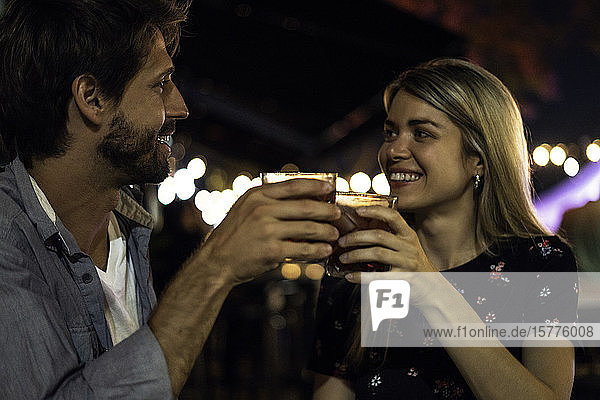 Junges Paar stößt mit Cocktailgläsern in einem Straßencafé an