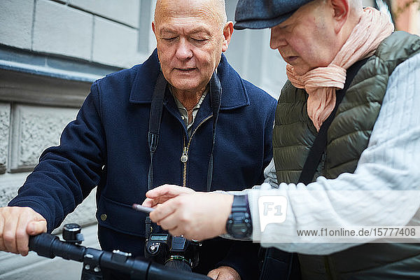 Älterer Mann zeigt einem Freund sein Handy  während er in der Stadt einen Roller hält