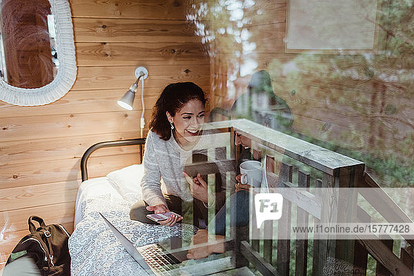Lächelnde Freundinnen mit Laptop auf dem Bett durch ein Glasfenster zu Hause