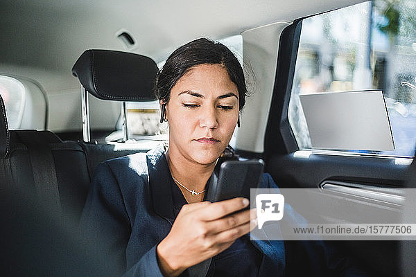 Businesswoman using smart phone while traveling in car