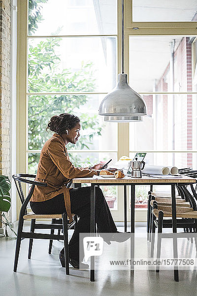 Selbstbewusste Architektin telefoniert  während sie zu Hause am Tisch sitzt