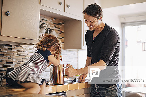 Happy father looking at daughter pushing french press while sitting on kitchen counter