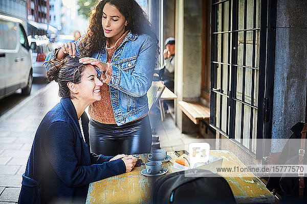 Lächelnde Frau lässt sich von einem Freund frisieren  während sie in einem Straßencafé in der Stadt sitzt
