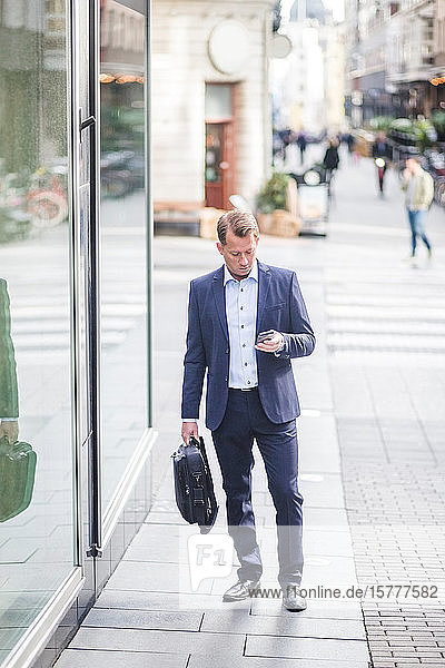 Mature businessman using smart phone while standing in city