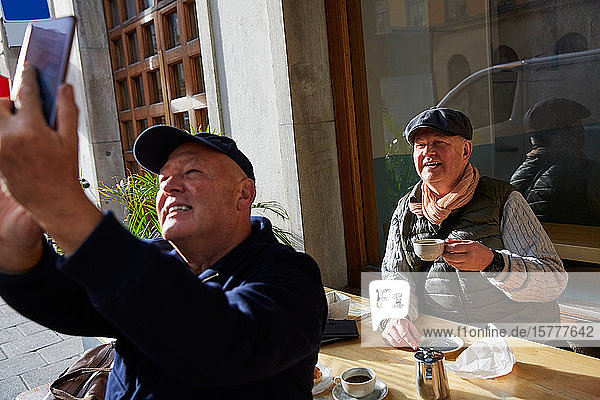 Lächelndes schwules Pärchen  das sich mit dem Handy selbstständig macht  während es im Straßencafé sitzt