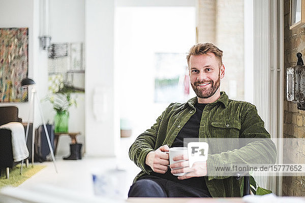 Porträt eines lächelnden männlichen Unternehmers mit Tasse im Heimbüro sitzend