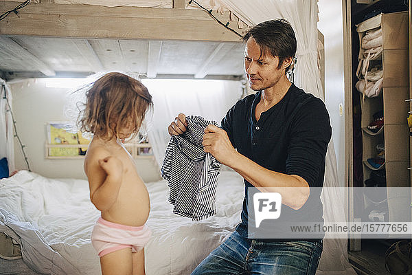 Father dressing daughter in bedroom