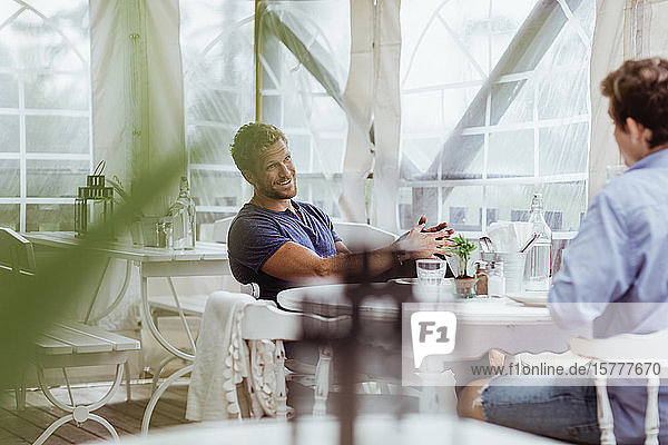 Smiling man talking with male friend while sitting in restaurant