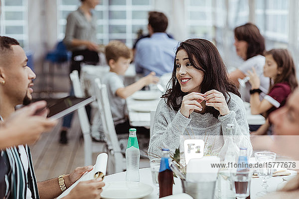 Lächelnde Frau unterhält sich mit einem männlichen Freund  während sie im Restaurant sitzt
