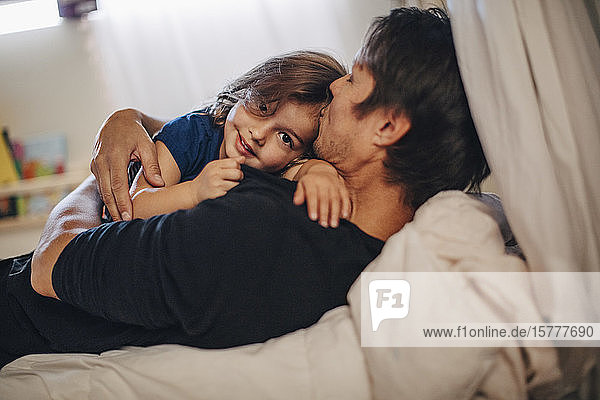 Portrait of smiling girl with mature father lying on bed